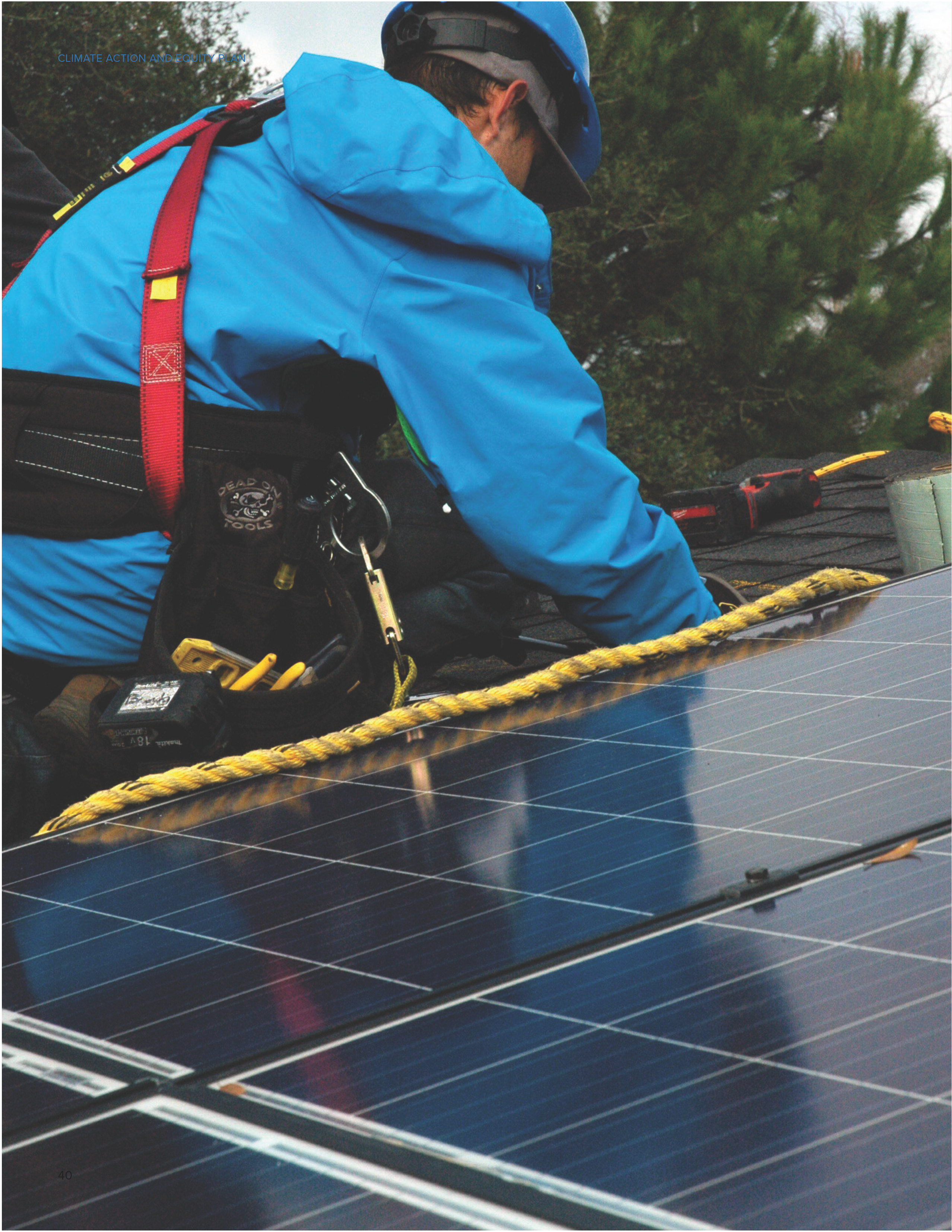 A worker in a blue jacket installs solar panels on a rooftop, showcasing solar cells and safety equipment.