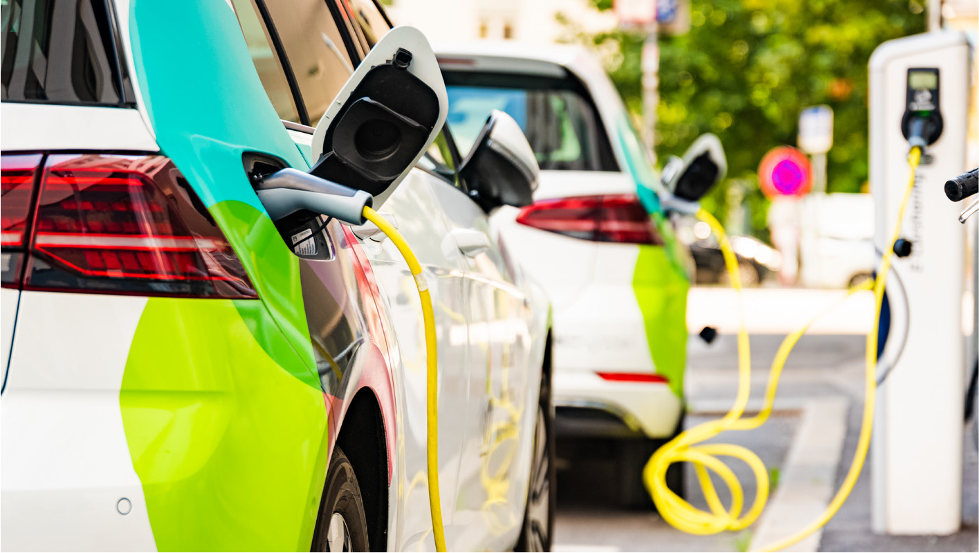 Two electric vehicles charging at a public station, with visible charging cables and colorful designs on the cars.