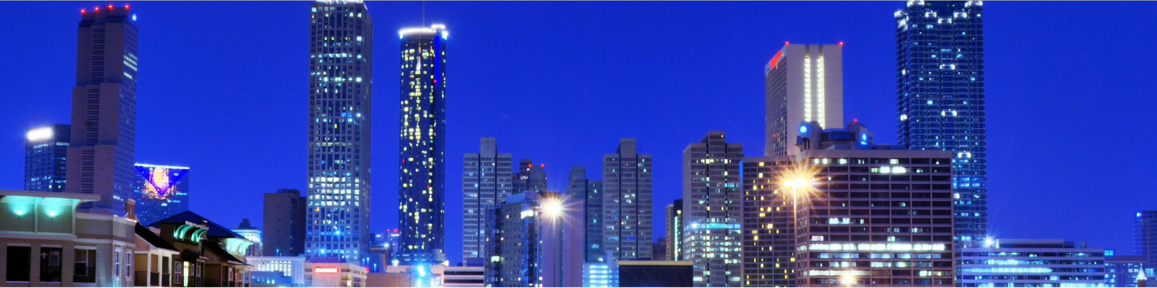 City skyline at night, featuring illuminated skyscrapers against a deep blue sky.