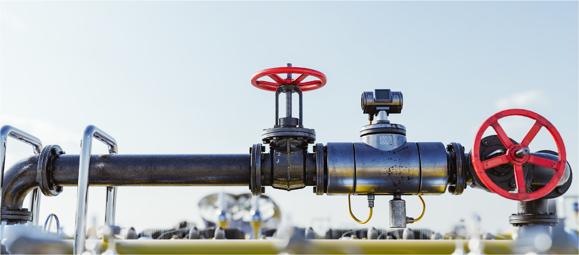 Close-up of industrial pipes with red valves and a flow meter against a clear sky.