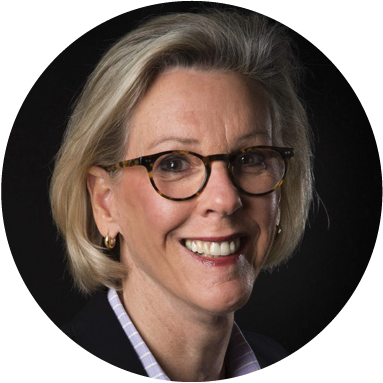 Close-up portrait of a smiling woman with blonde hair and glasses, set against a dark background.