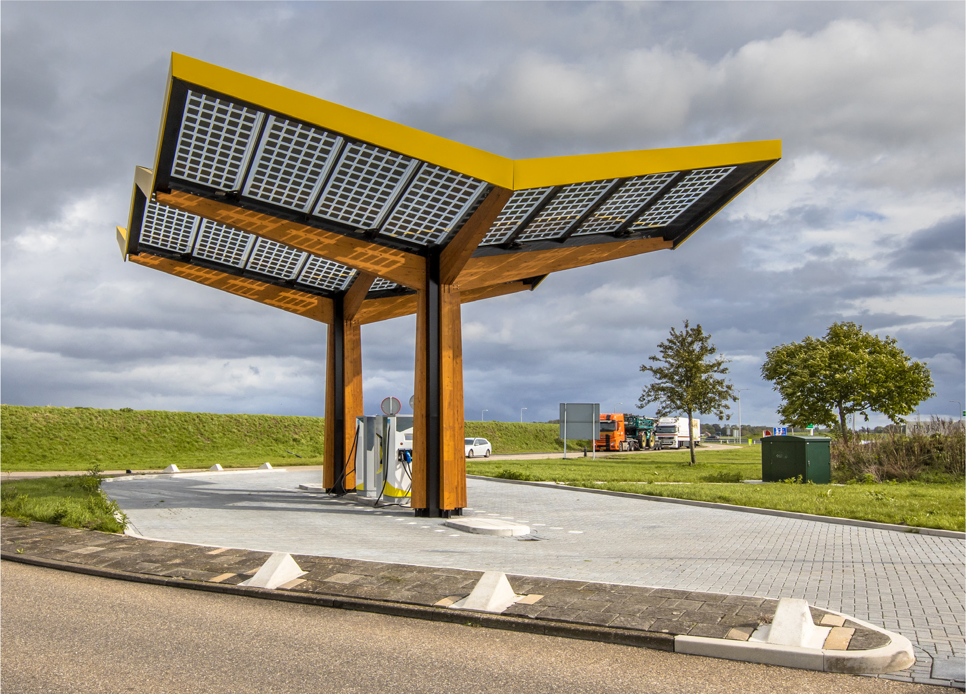Modern solar-powered charging station with a distinctive roof design, set against a cloudy sky and grassy backdrop.