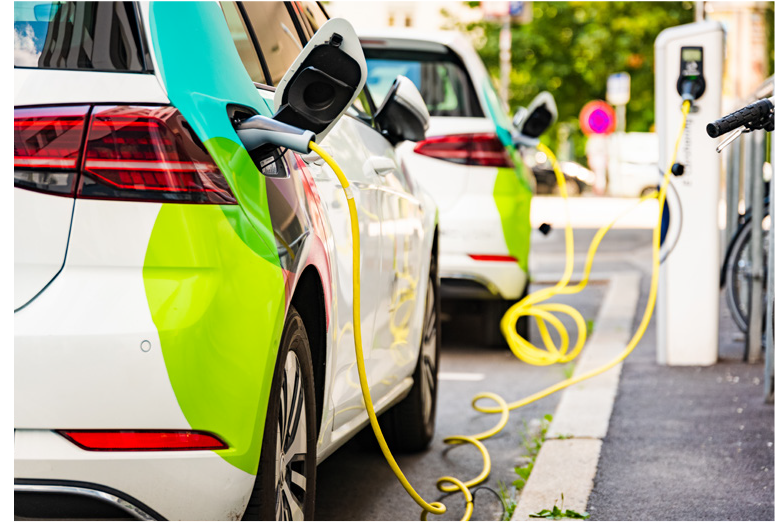 Two electric cars charging at a public station, with yellow charging cables connected to the vehicles.