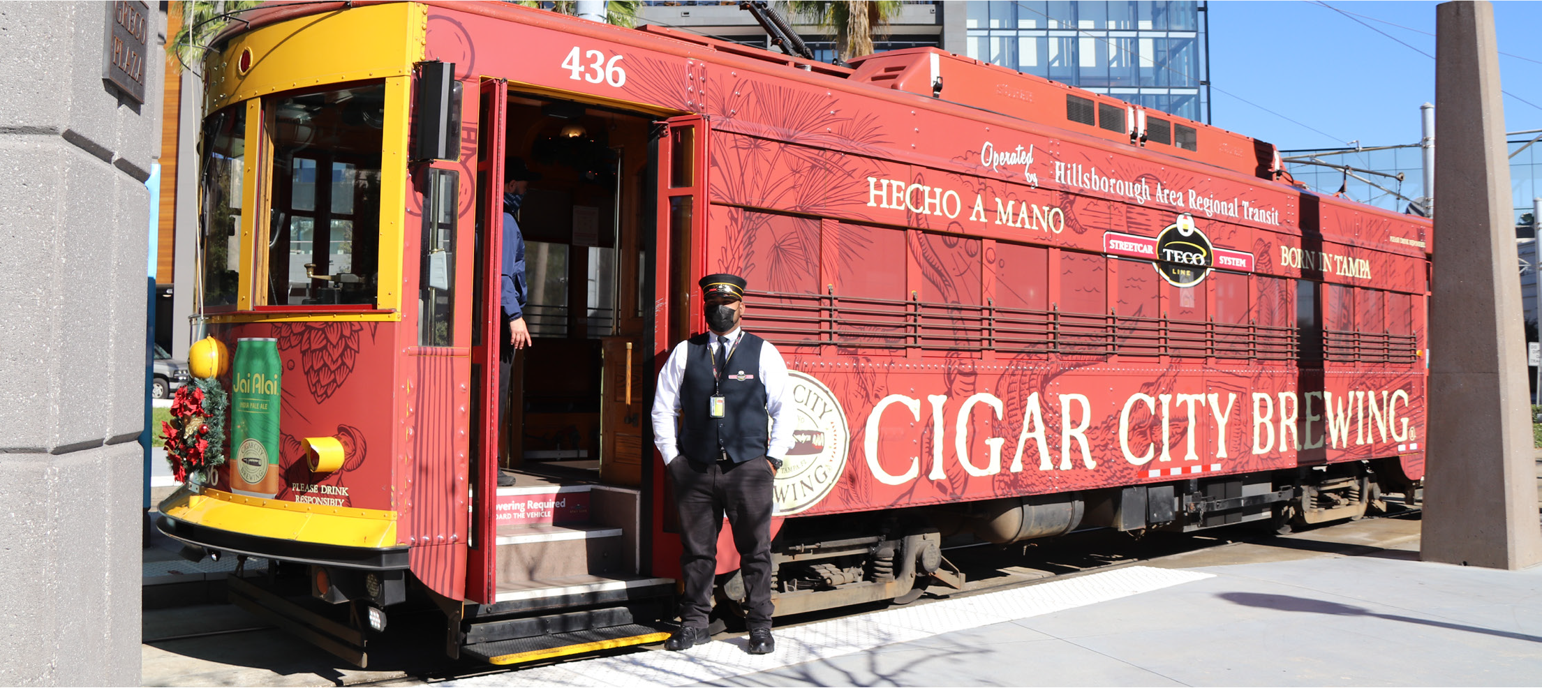 A vintage red streetcar with a conductor standing next to it, promoting Cigar City Brewing.