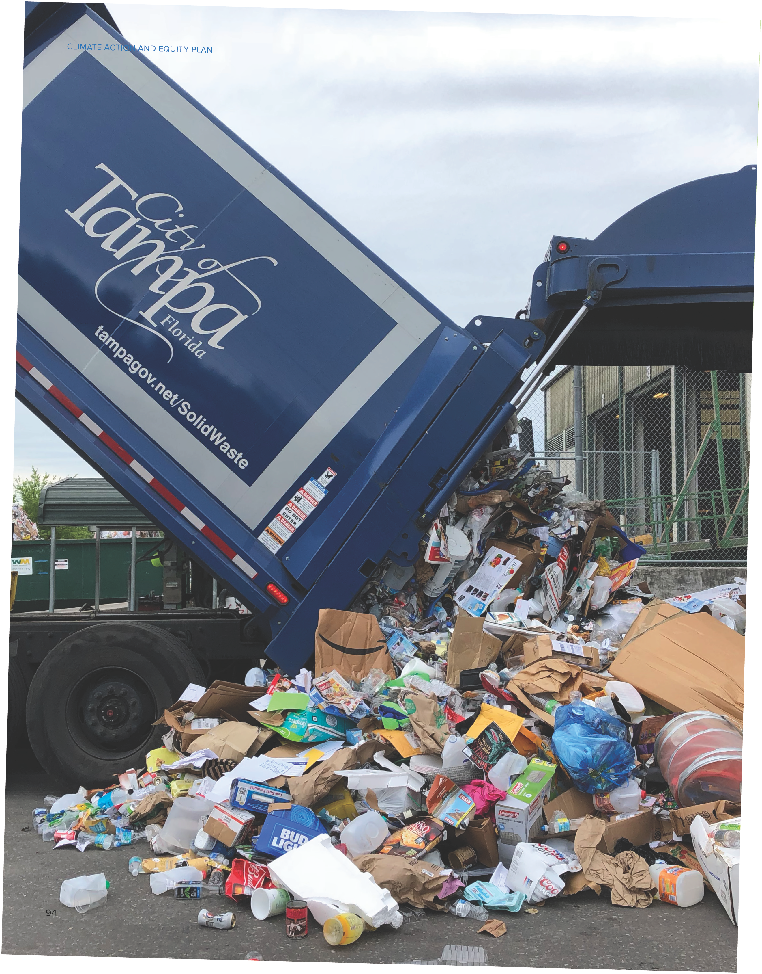 A garbage truck dumping a large pile of mixed waste, including plastic, cardboard, and other refuse, onto the ground.
