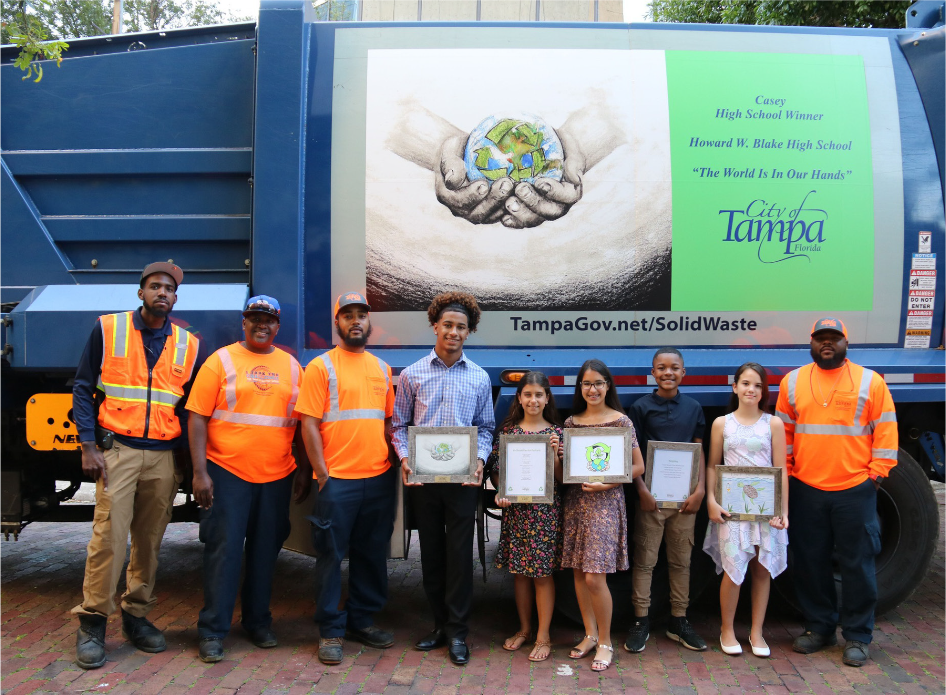 Group of students holding art awards in front of a Tampa waste truck, promoting environmental awareness.