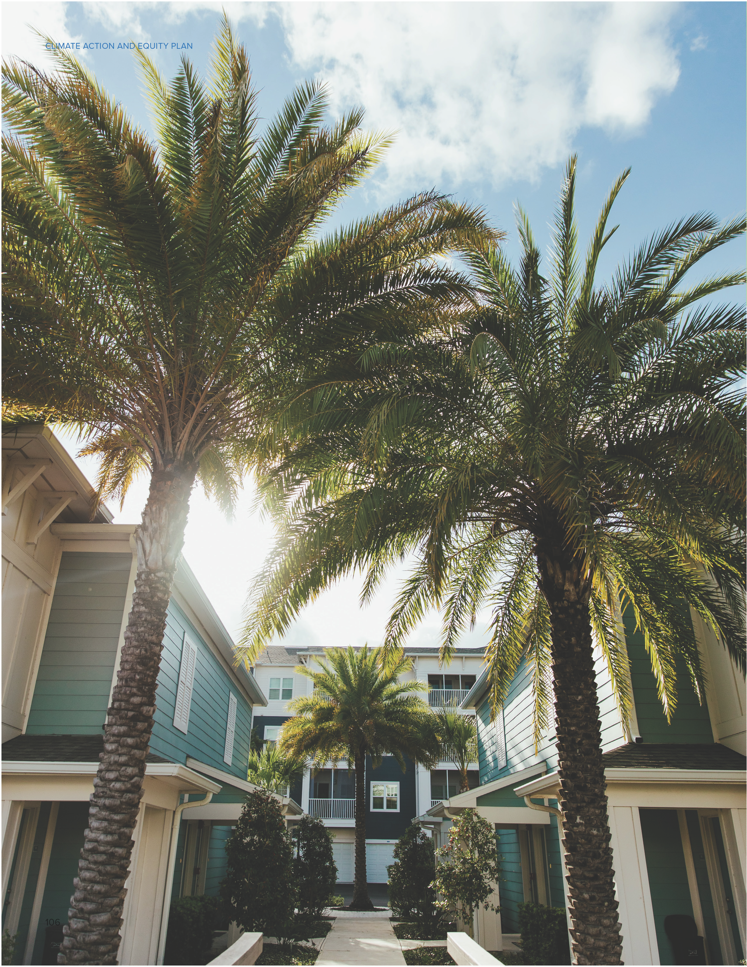 Palm trees frame a walkway between colorful residential buildings under a partly cloudy sky.