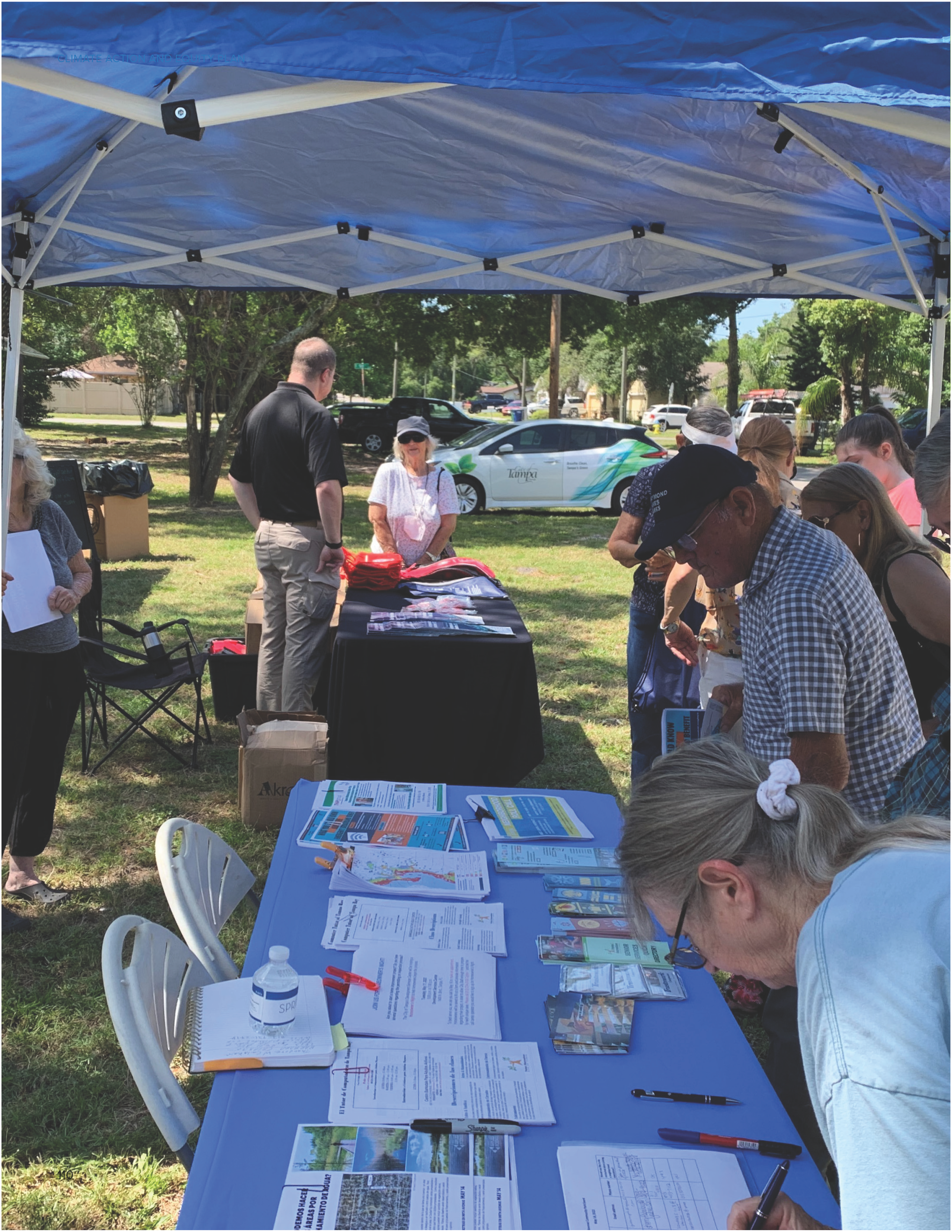People gathered under a tent reviewing brochures and signing up for information at an outdoor event.