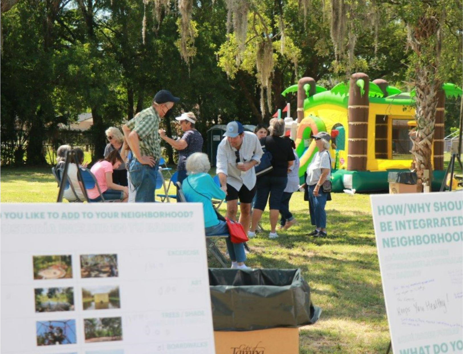 Community event with people discussing neighborhood improvements, outdoor seating, and a bounce house in the background.