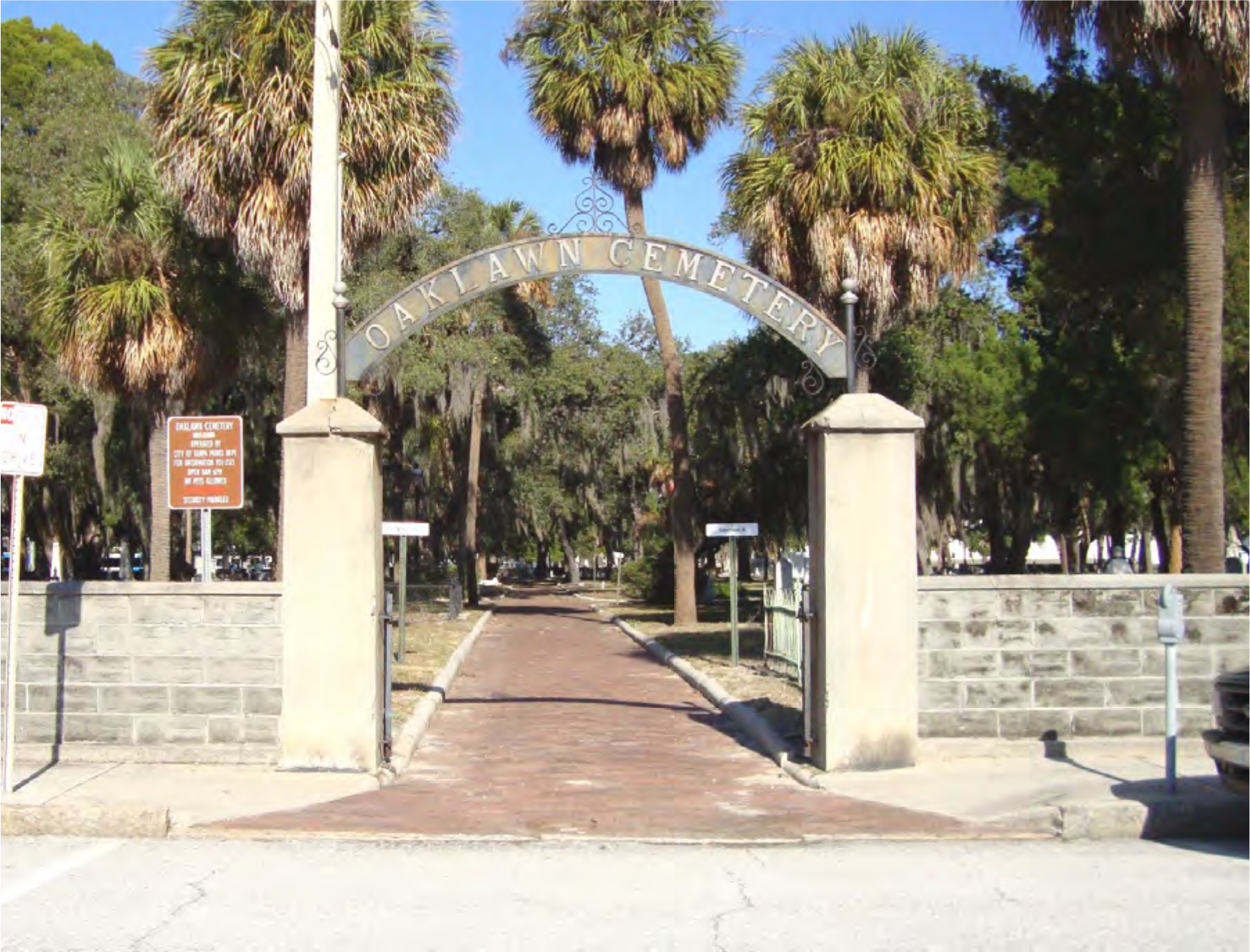 Entrance to Oaklawn Cemetery with stone pillars and palm trees lining the pathway.