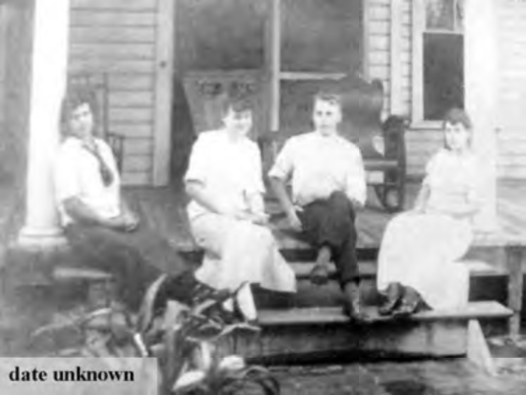 Four people sitting on a porch, with a plant in foreground; historical photo, date unknown.