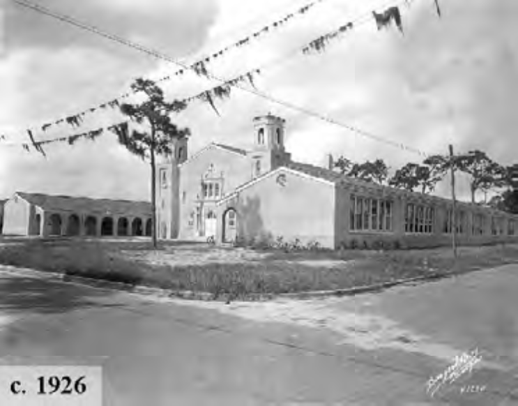 Historic building from 1926, showcasing a main structure with towers and arched windows, surrounded by grass and utility wires.