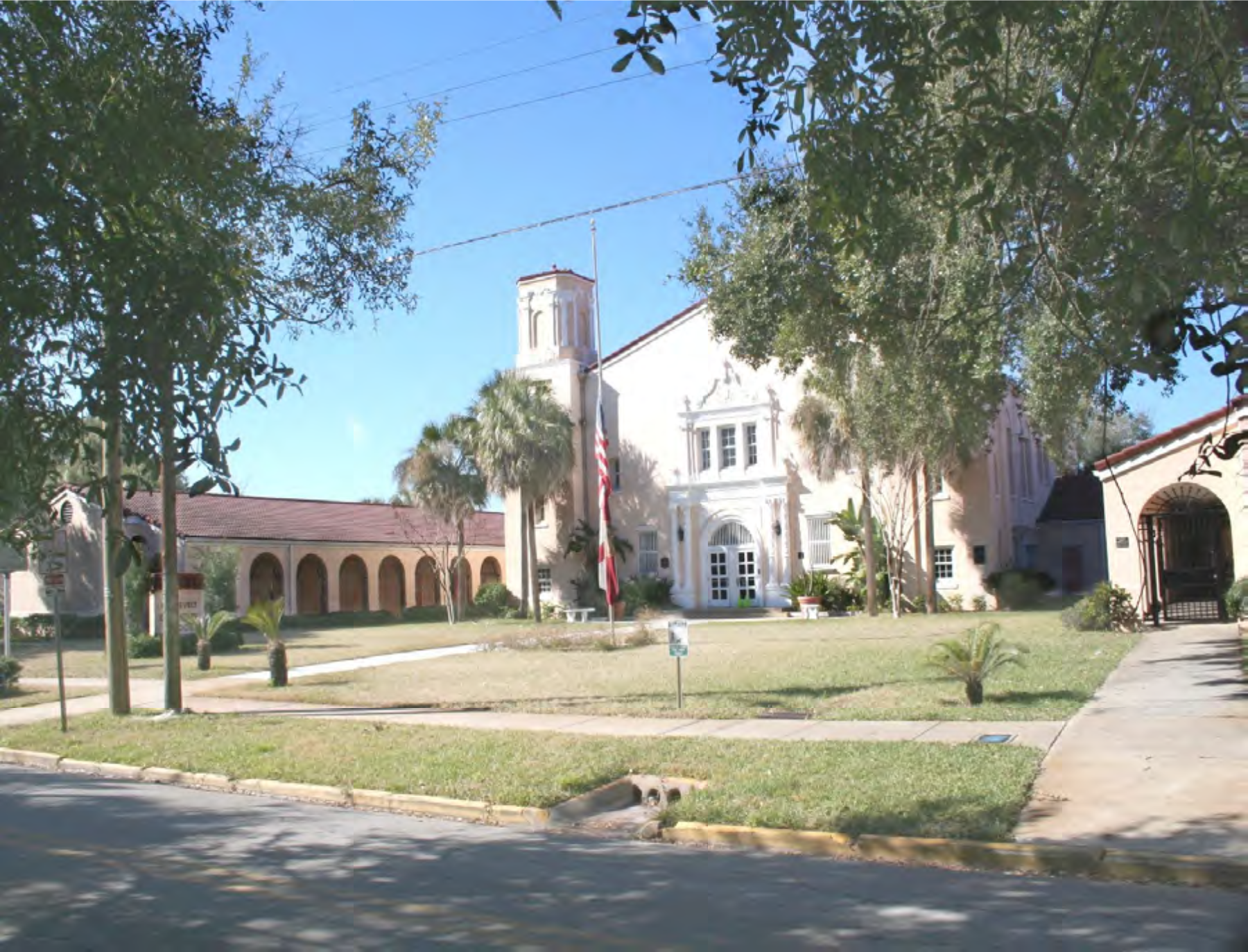 A building with a tower and palm trees in front, set against a clear blue sky.