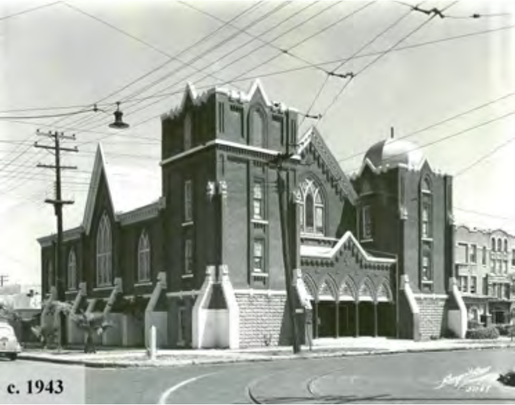 Historic building from 1943, featuring Gothic architectural elements, set on a street with utility poles and wires.