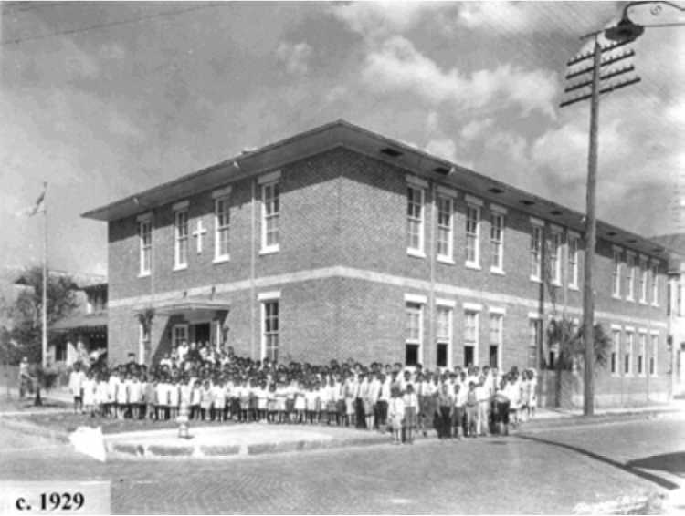 Historic black-and-white image of a large group of children and adults in front of a brick school building, circa 1929.