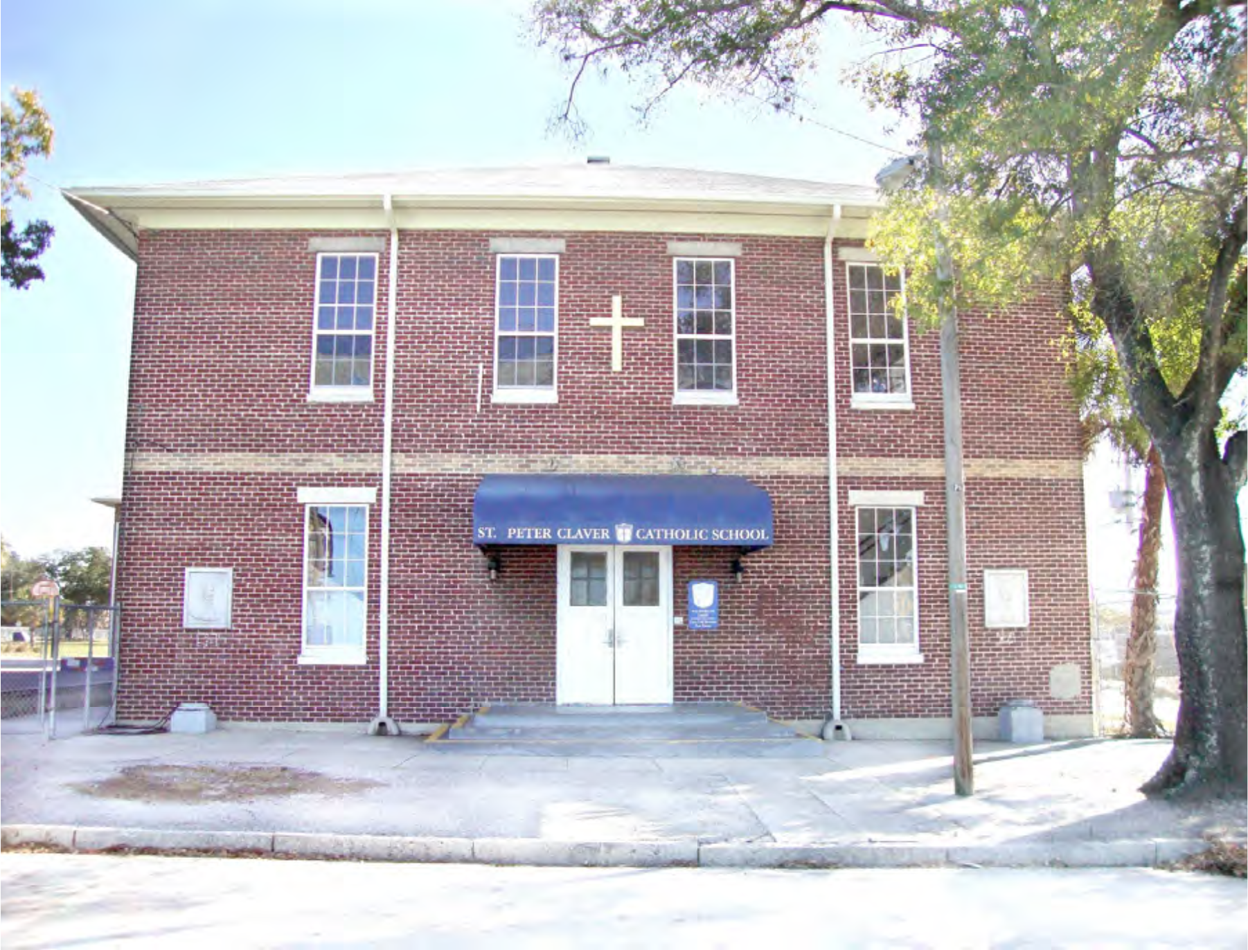 Front view of St. Peter Claver Catholic School, a brick building with a cross and blue awning.