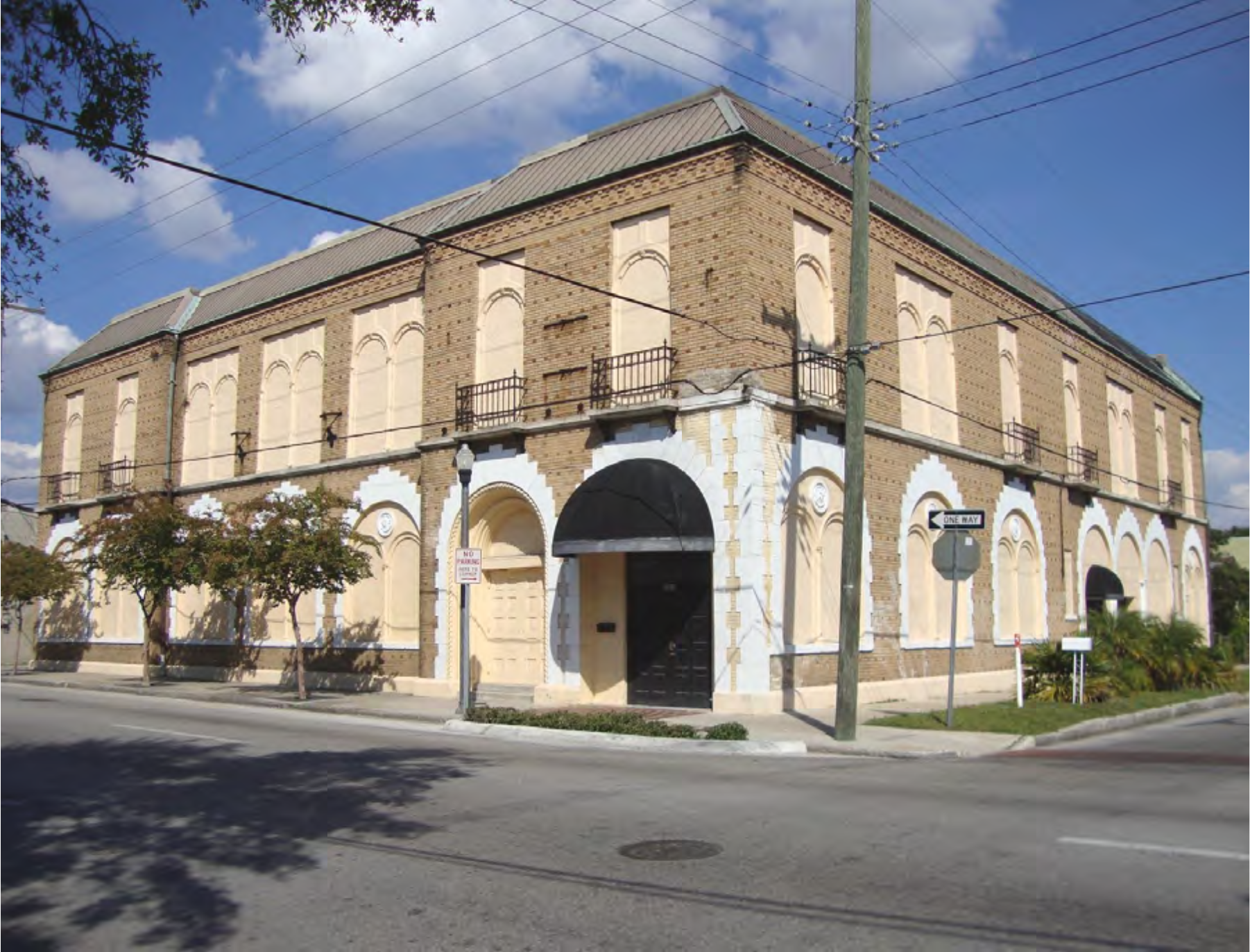 Historic brick building with arched windows and a black entrance, located on a street with sidewalks and trees.