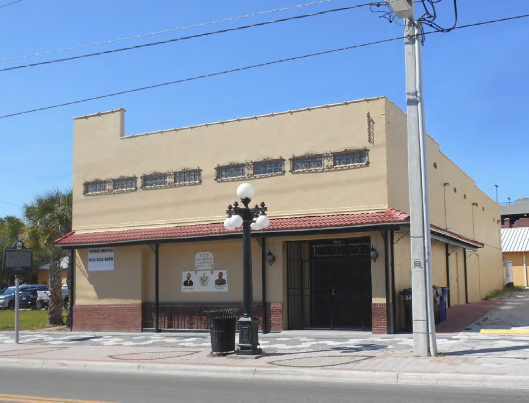A beige building with decorative windows, located on a street with a sidewalk and street lamps, under a clear blue sky.