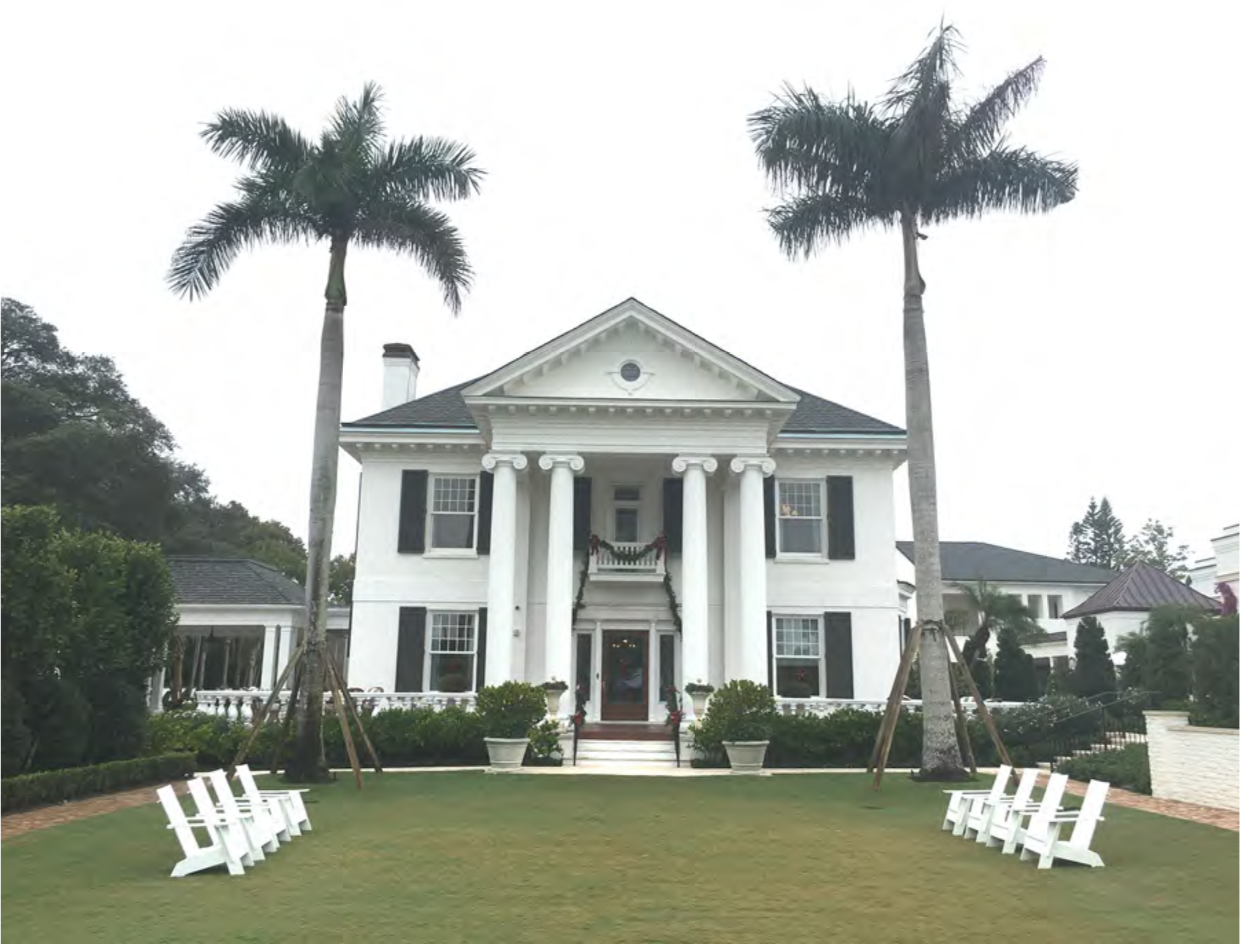 A large white mansion with columns, surrounded by palm trees and green lawn, featuring a welcoming entrance.