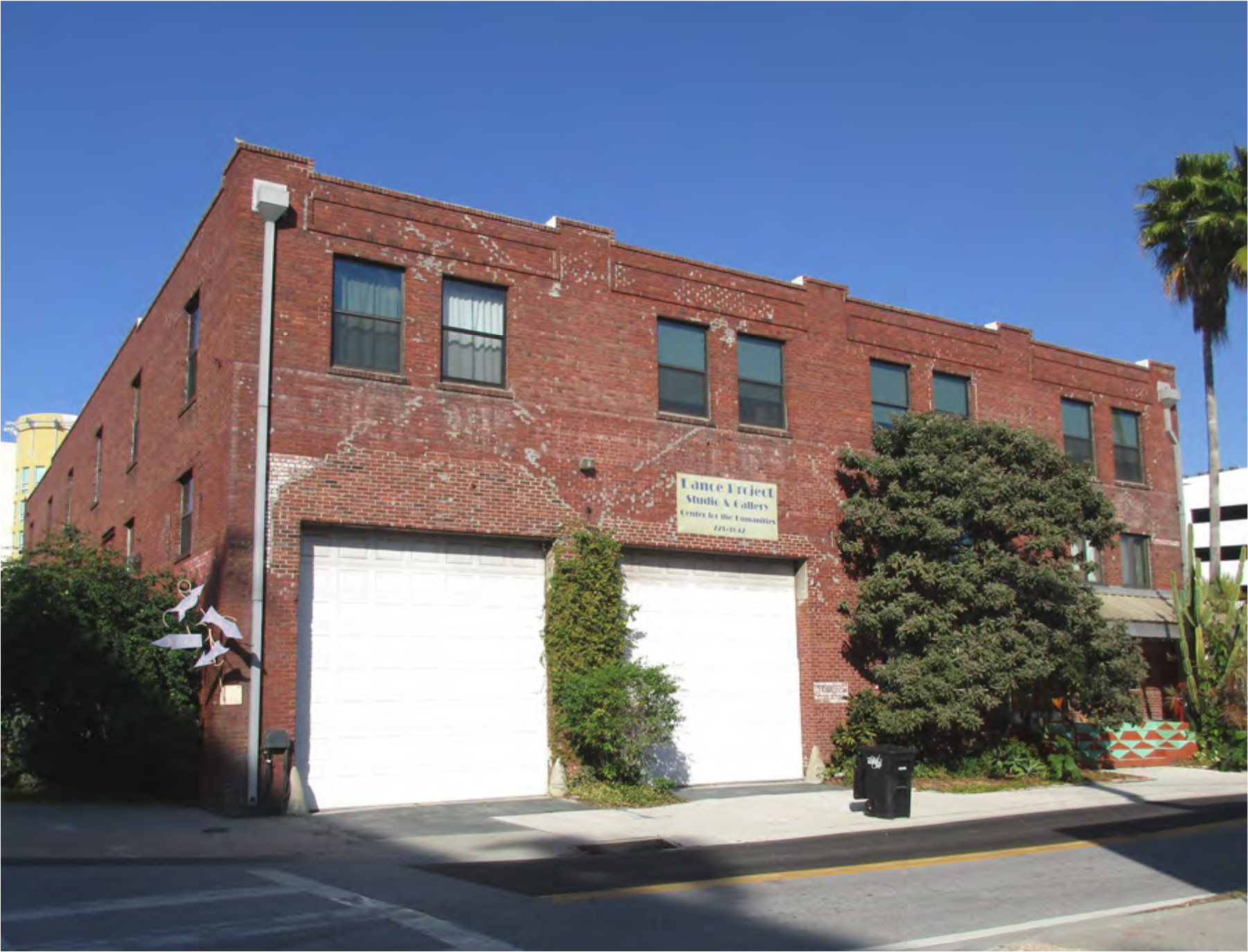Red brick building with two garage doors, palm trees, and a sign that reads 'Lennon & Ewert.' Clear blue sky in the background.