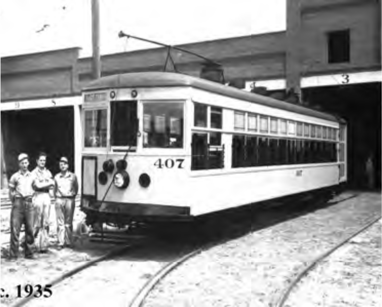 A vintage streetcar numbered 407, with three men standing beside it at a depot, circa 1935.