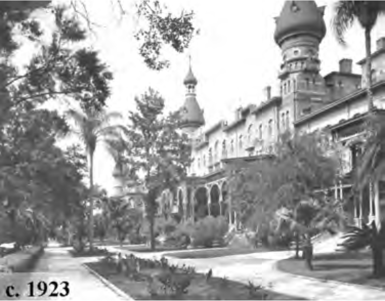 Historic black and white photo of a grand building with towers, surrounded by trees and pathways, dated circa 1923.