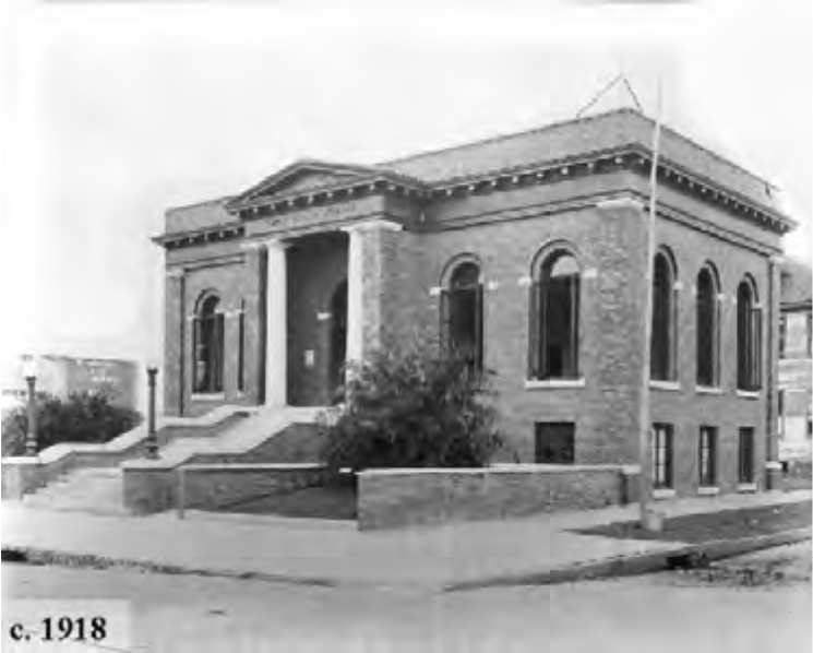 Historic brick building from around 1918, featuring a grand entrance and large windows, situated on a corner lot.