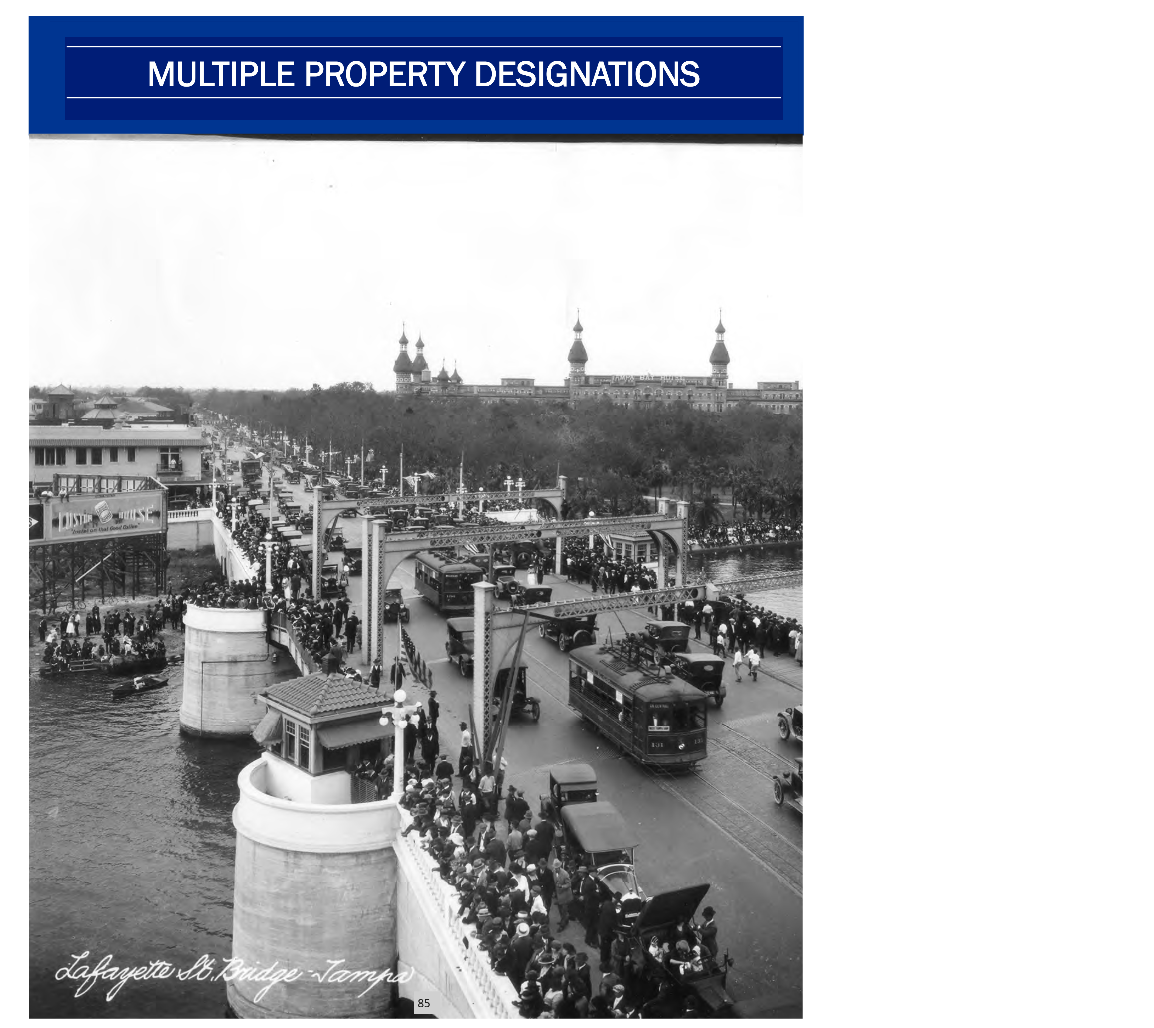 Historic black and white photo of a busy bridge with people, vehicles, and buildings in the background.