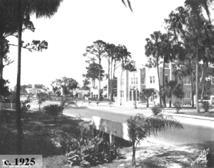 Historical black and white image of a street lined with trees and buildings, dating circa 1925.