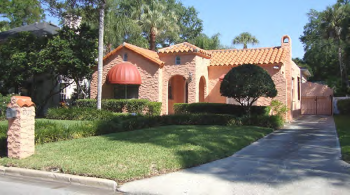 Single-story pink house with terracotta roof, red awning, manicured lawn, and palm trees in front.