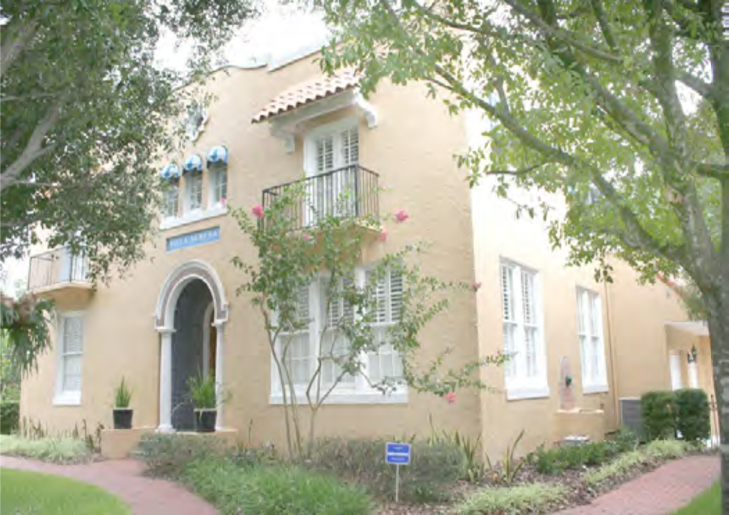 A charming yellow building with arched entrance and blue awnings, surrounded by greenery and flowering plants.