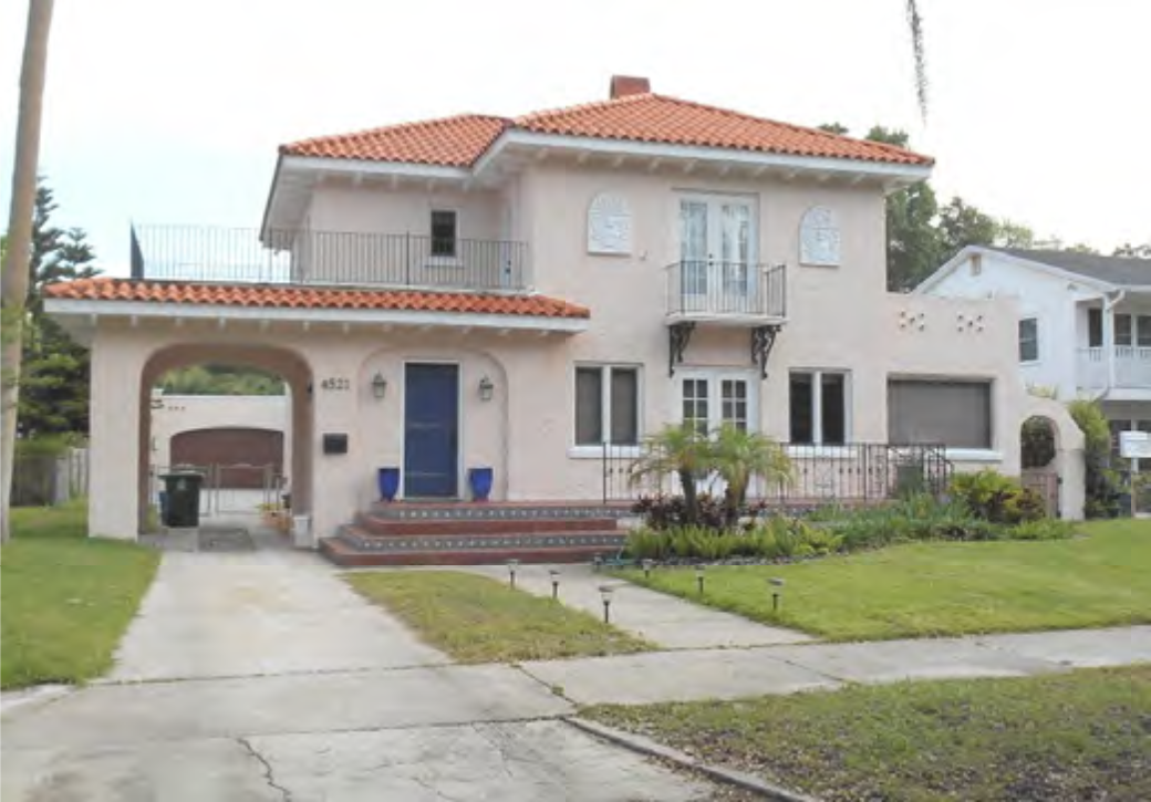 Pink two-story house with a tiled roof, balconies, and a manicured lawn in a residential neighborhood.
