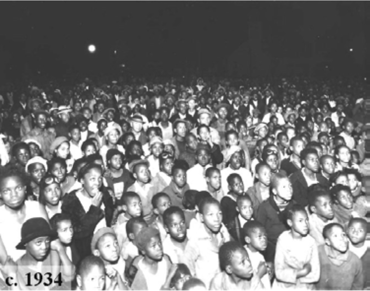 A large crowd of children and adults gathered outdoors, likely at an event, in a black and white photograph from around 1934.