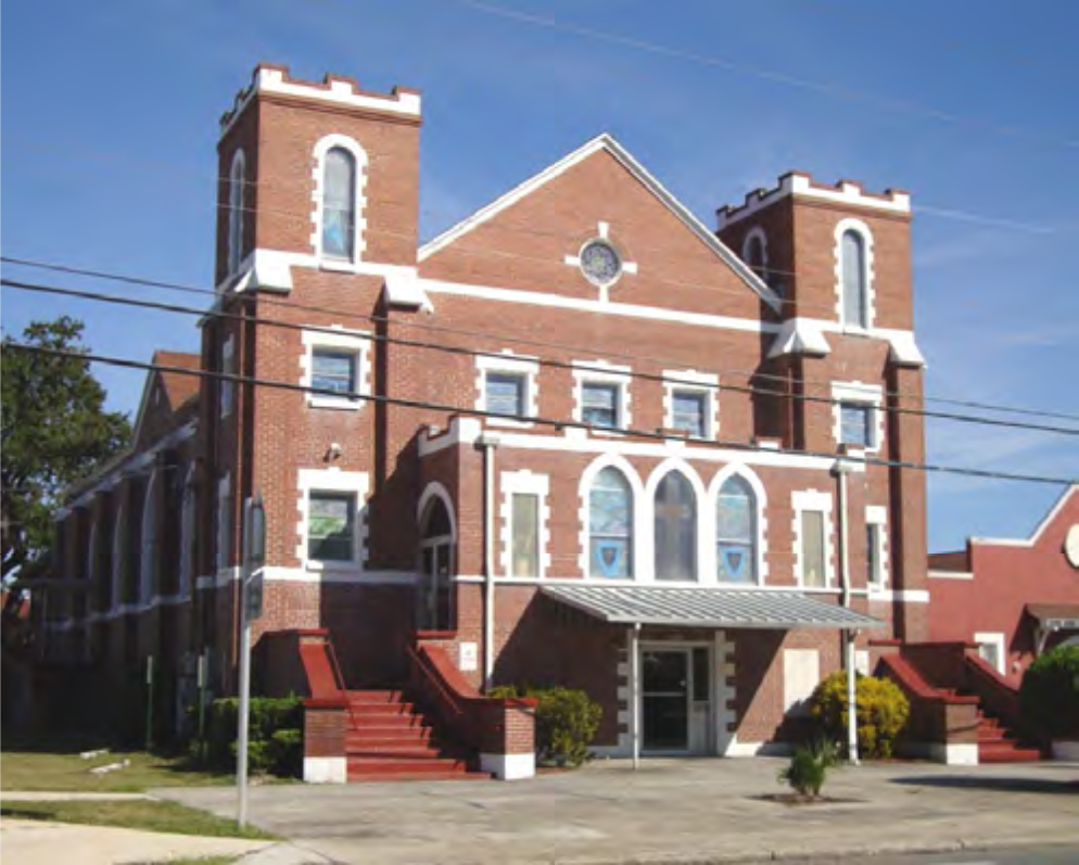 Historic brick building with twin towers, arched windows, and a prominent entrance, set against a clear blue sky.