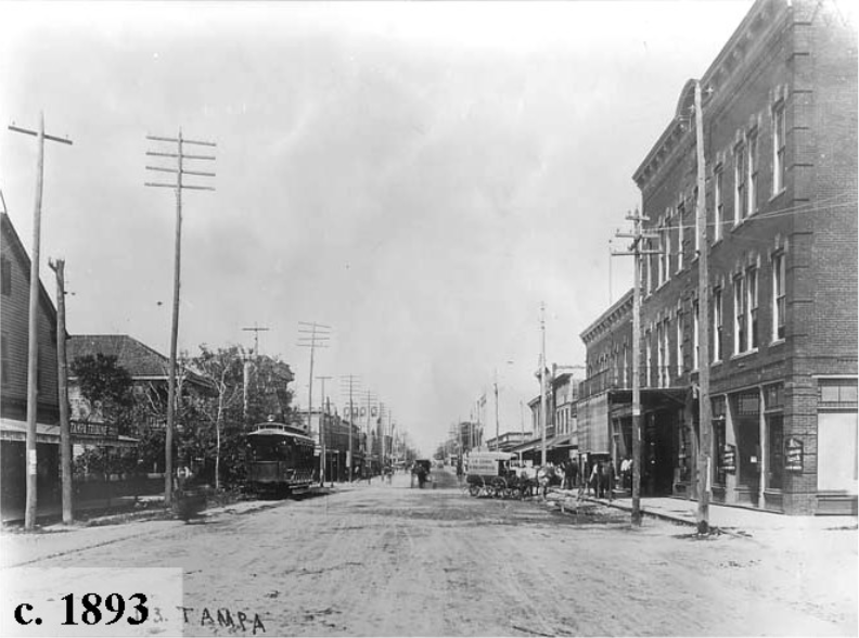 Historic black-and-white photo of a street in Tampa, circa 1893, showing horse-drawn carriages and early electric streetcars.