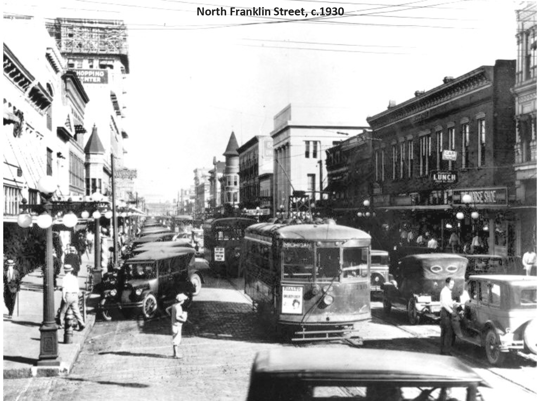 Historic black and white photo of North Franklin Street, c. 1930, featuring streetcars and early automobiles.