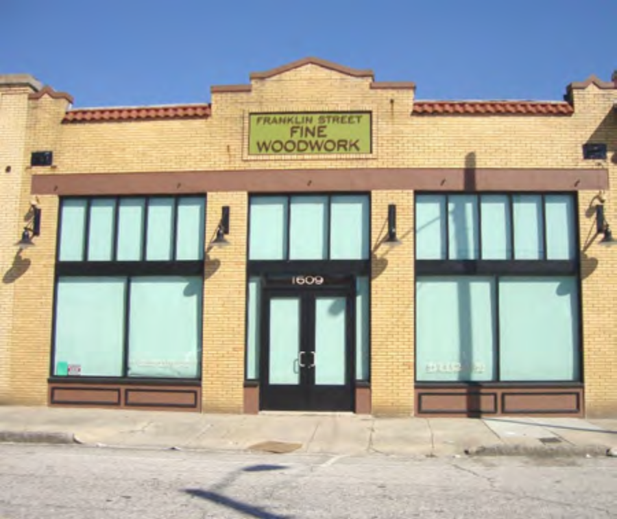 Front view of a brick building with large windows, featuring a sign for 'Franklin Street Fine Woodwork.'
