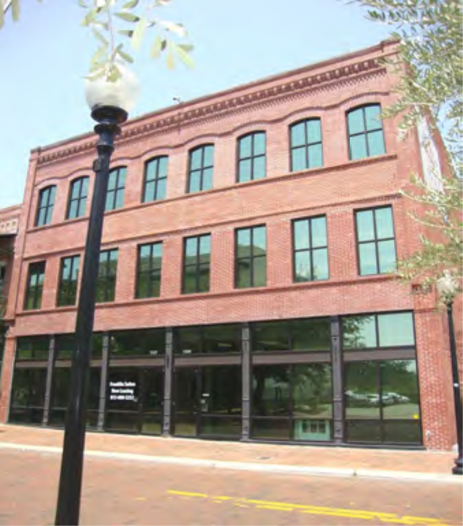 A three-story red brick building with large black-framed windows and a lamppost in the foreground.