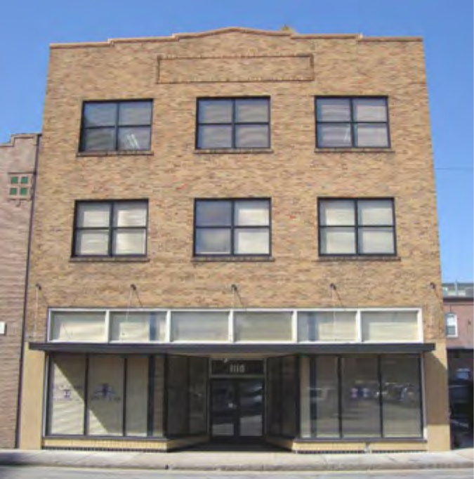 Facade of a three-story brick building with multiple windows and an empty storefront on the ground floor.