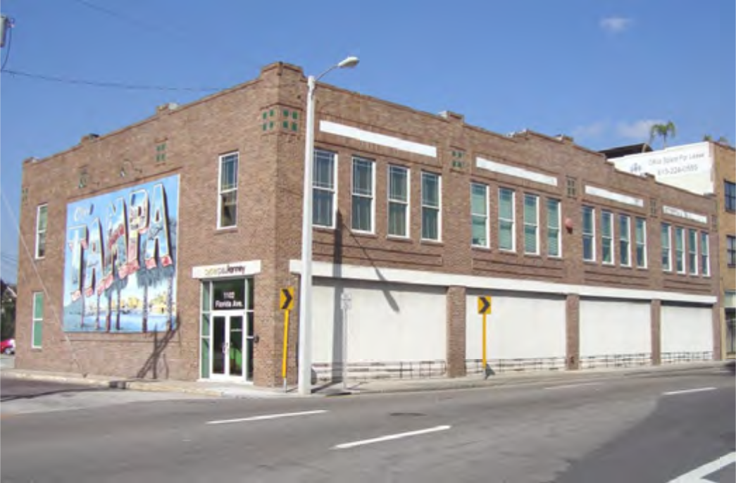 A brick building with large windows and a colorful mural on one side, located at a street corner.