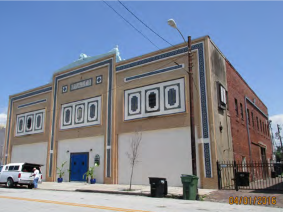 Exterior view of a historical building with decorative elements, featuring windows and a blue entrance on a sunny day.