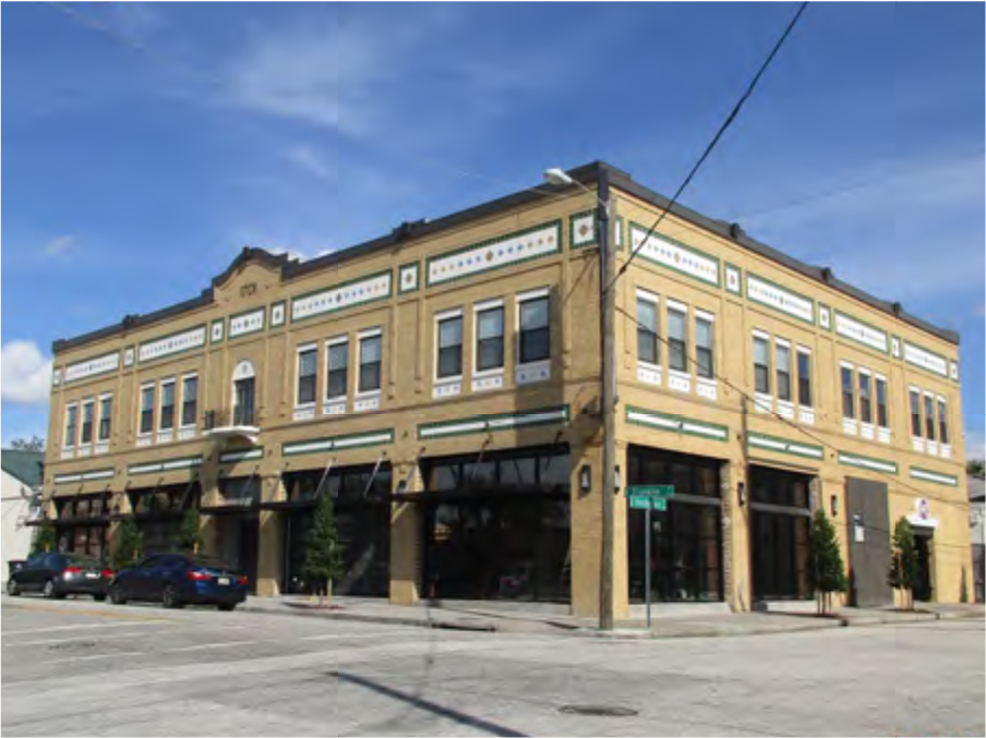 A historic brick building with green and white decorative elements, featuring large windows and a corner facade on a sunny day.