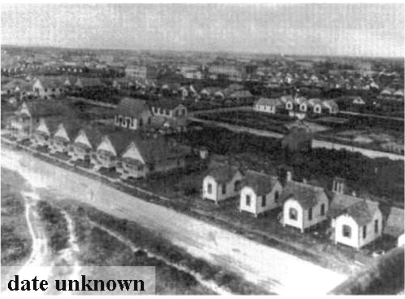 Aerial view of houses arranged in rows, with fields and additional structures in the background. Date unknown.