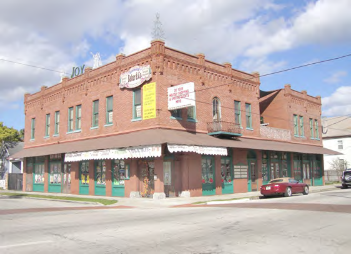 Historic red brick building with decorated windows and signs. Two stories with a balcony on the corner. Blue sky with clouds.