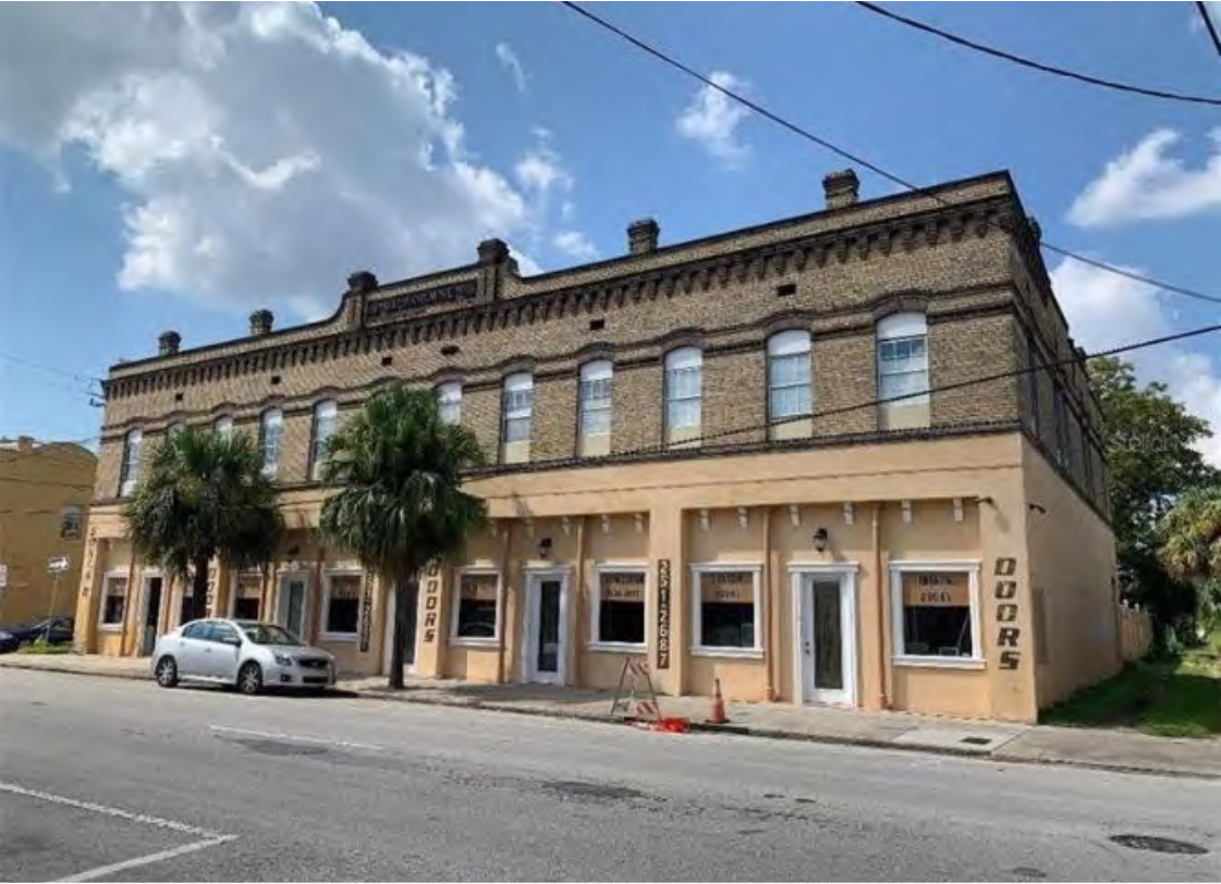 Historic brick building with multiple windows and palm trees, located on a street, featuring the word 'DOORS' on the facade.