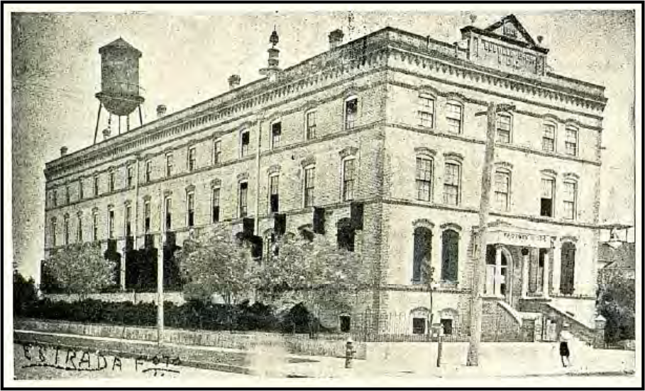 Historic building with a water tower, featuring multiple windows and stairs, surrounded by trees.