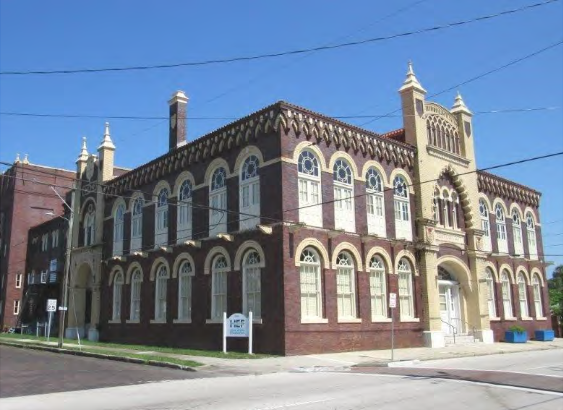 Historic brick building with ornate architecture and arched windows, featuring a distinct gable roof against a clear blue sky.