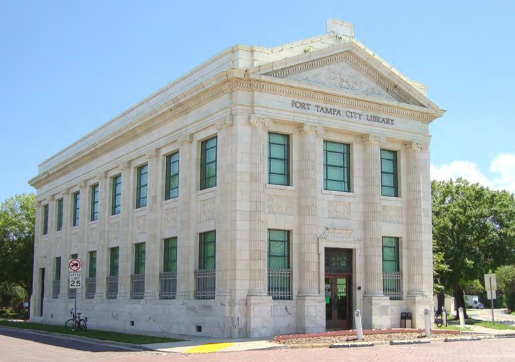 Historic Port Tampa City Library building with white columns and green windows, surrounded by trees and a clear blue sky.