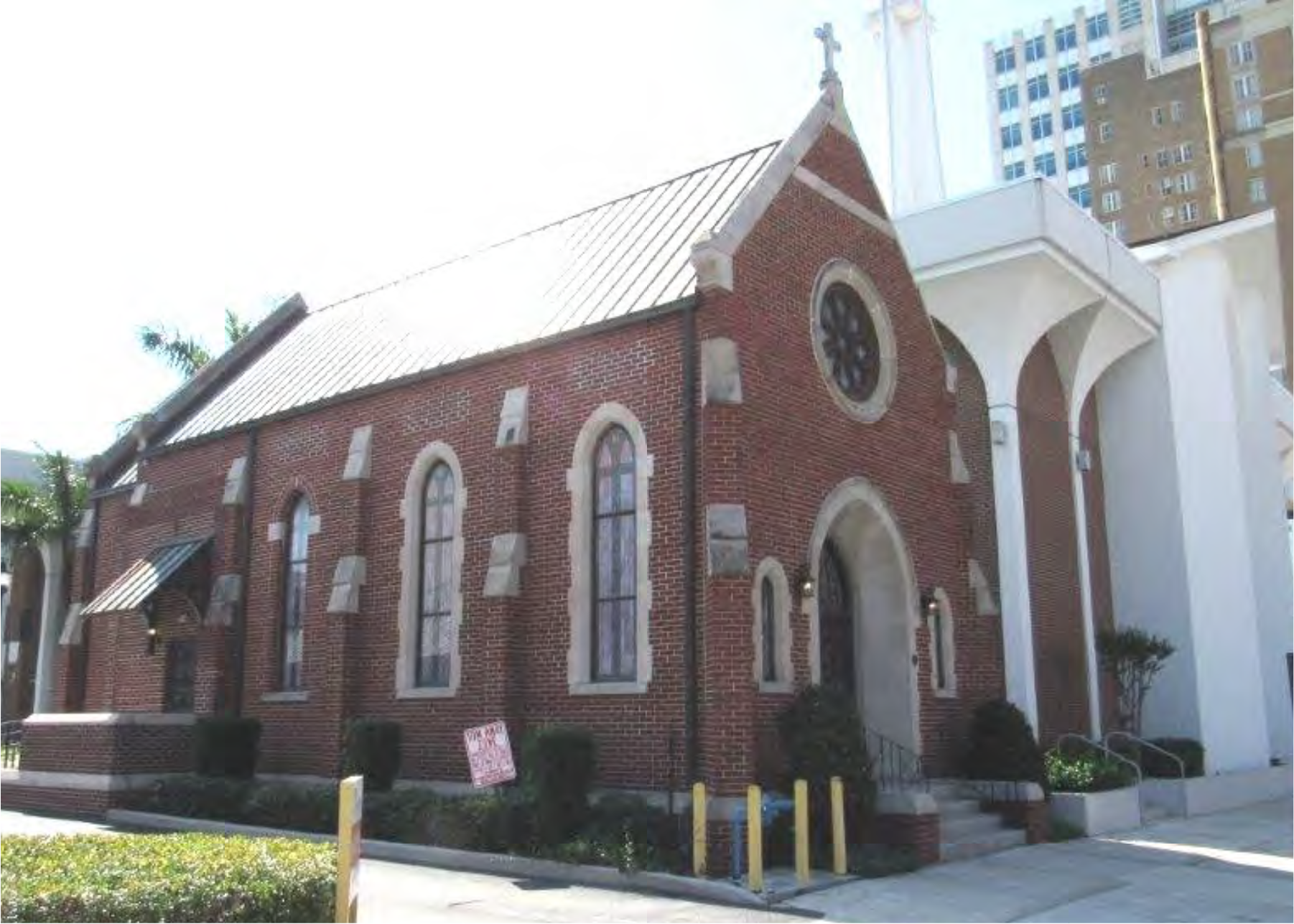 Historic brick church with arched windows and a steep roof, adjacent to a modern building in a city setting.