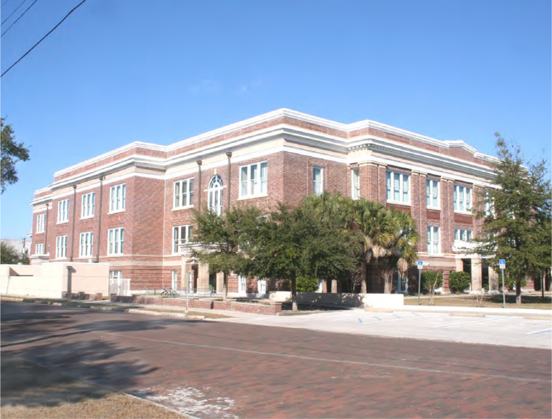 A large brick building with decorative elements, surrounded by trees and a clear blue sky, located on a quiet street.